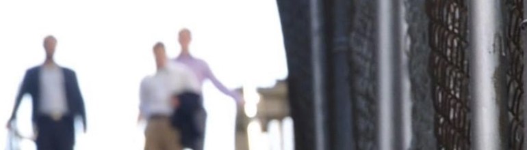 Three blurred figures climbing a stairway into white daylight, a chain-link fence running alongside.